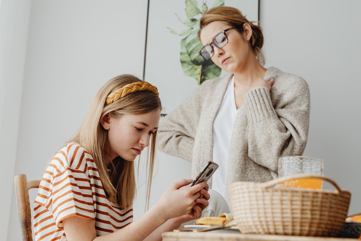 A mother talking with her daughter, who is looking at her phone at the breakfast table