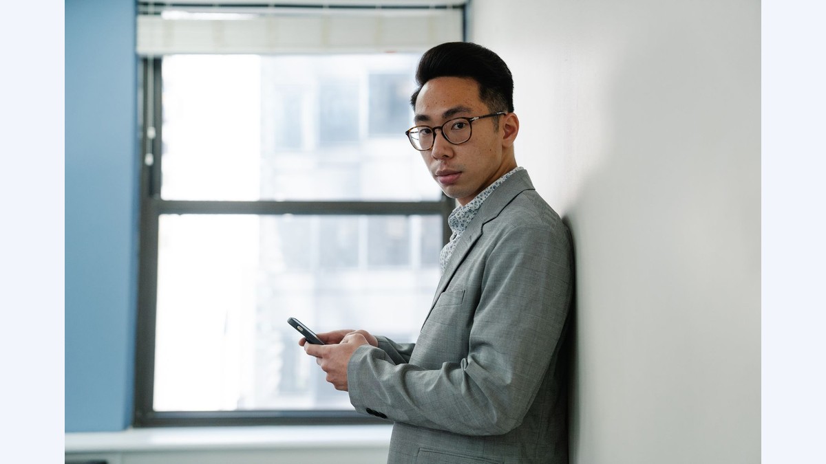 A man leaning against a wall looking down at his phone, about to turn off Gmail smart features