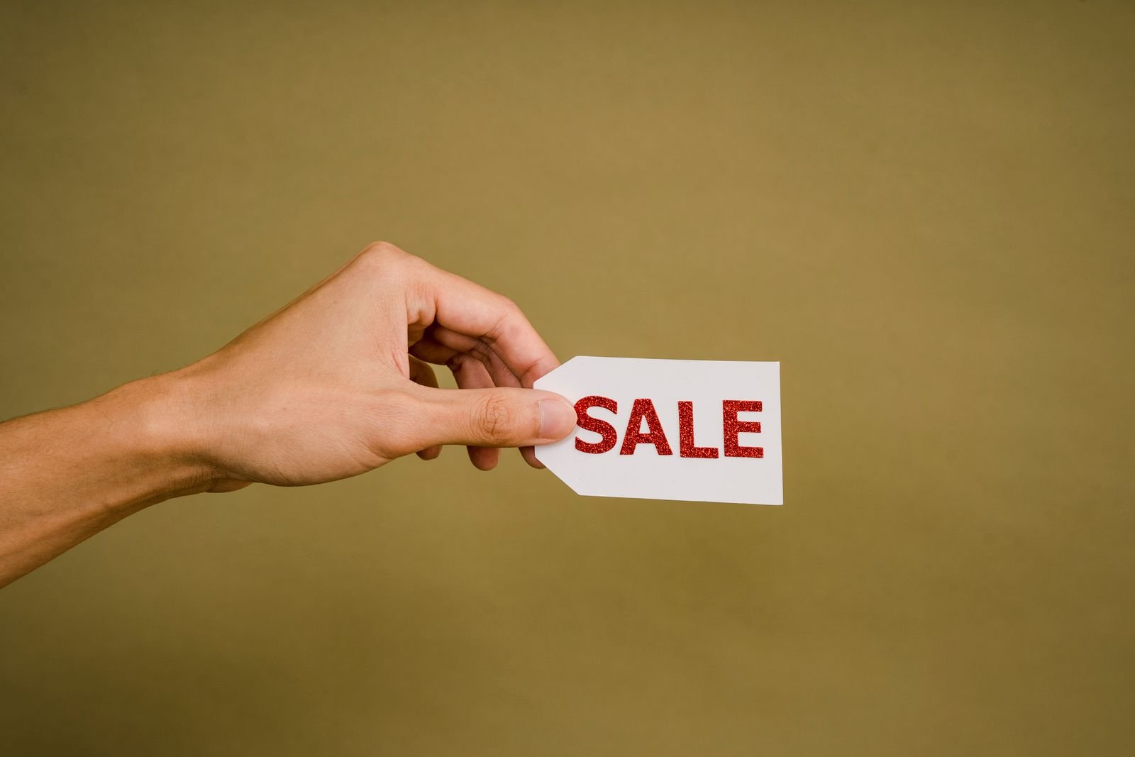 A hand holding a small white sale tag, for the section on how to spend less while memory prices stay high